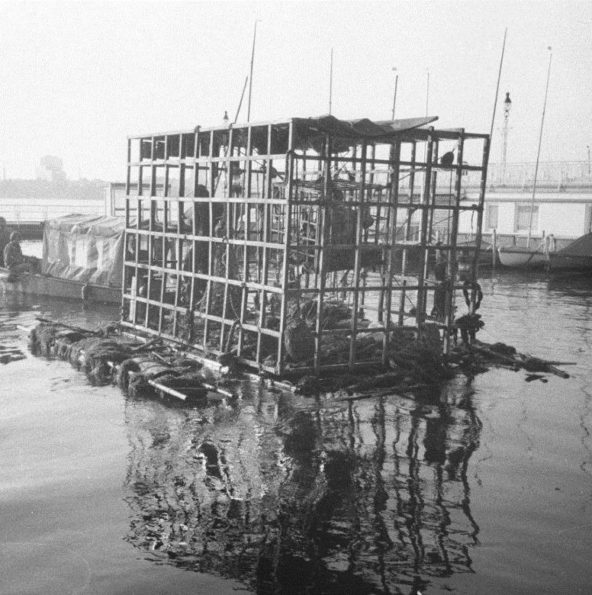 Une cage dans laquelle est enfermé un personnage flotte sur un lac