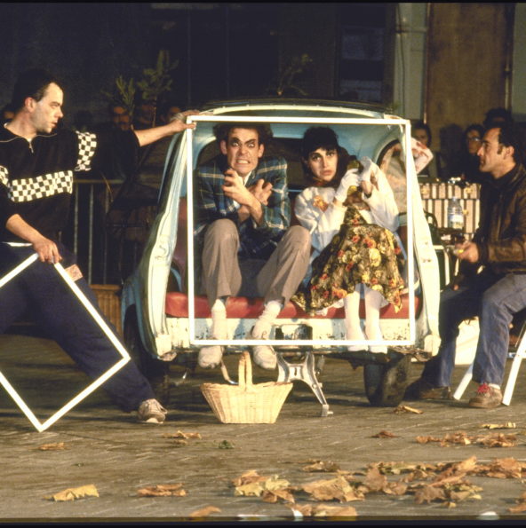 Le couple de comédien du Roman Photo est dans une voiture fiat, coupée en deux pour laisser voir l'intérieur. Les techniciens sont sur le côté de l'image et tiennent le cadre qui représente la scène du Roman photo